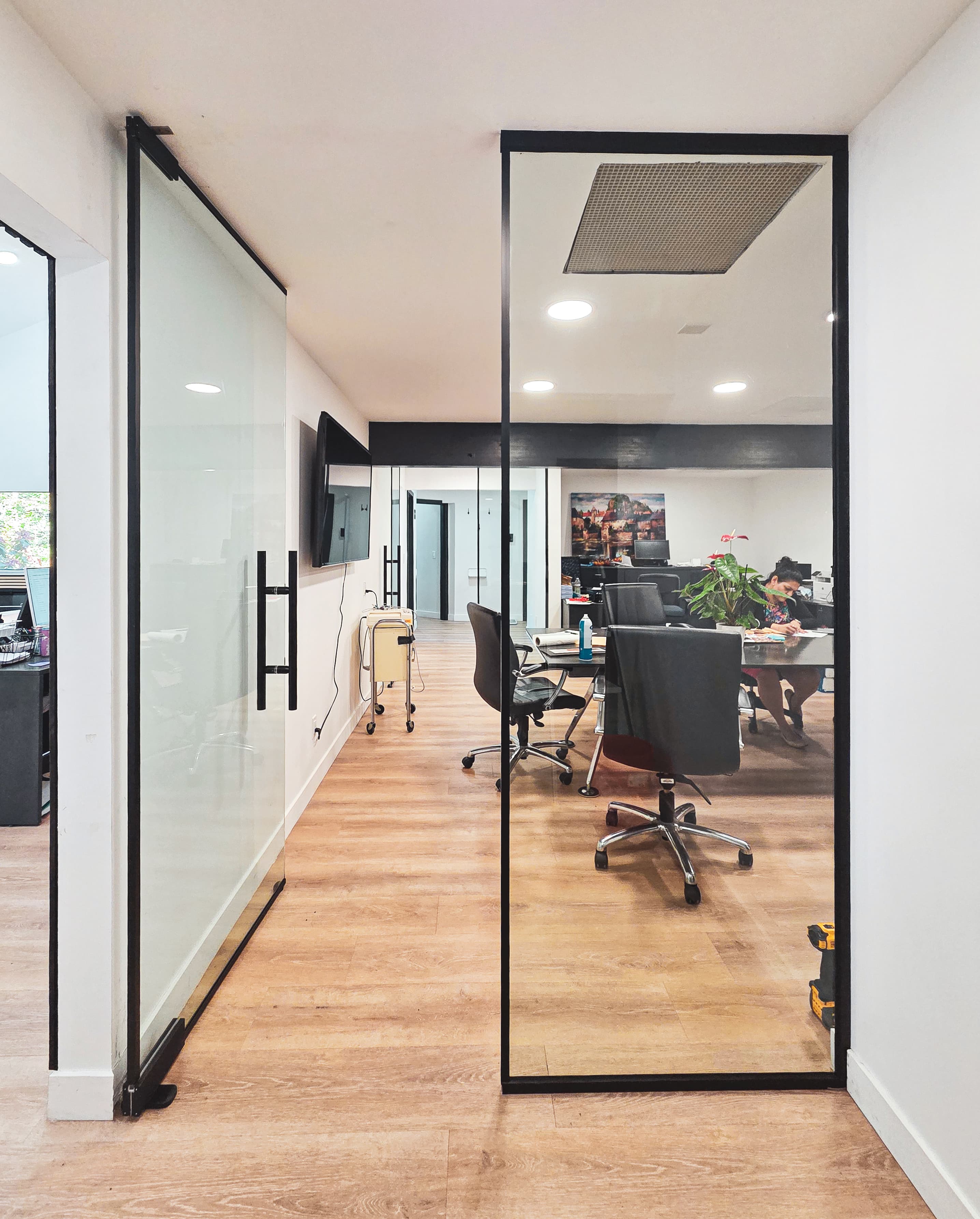 Modern office space with a black framed glass sliding door, wood floors, and meeting area.