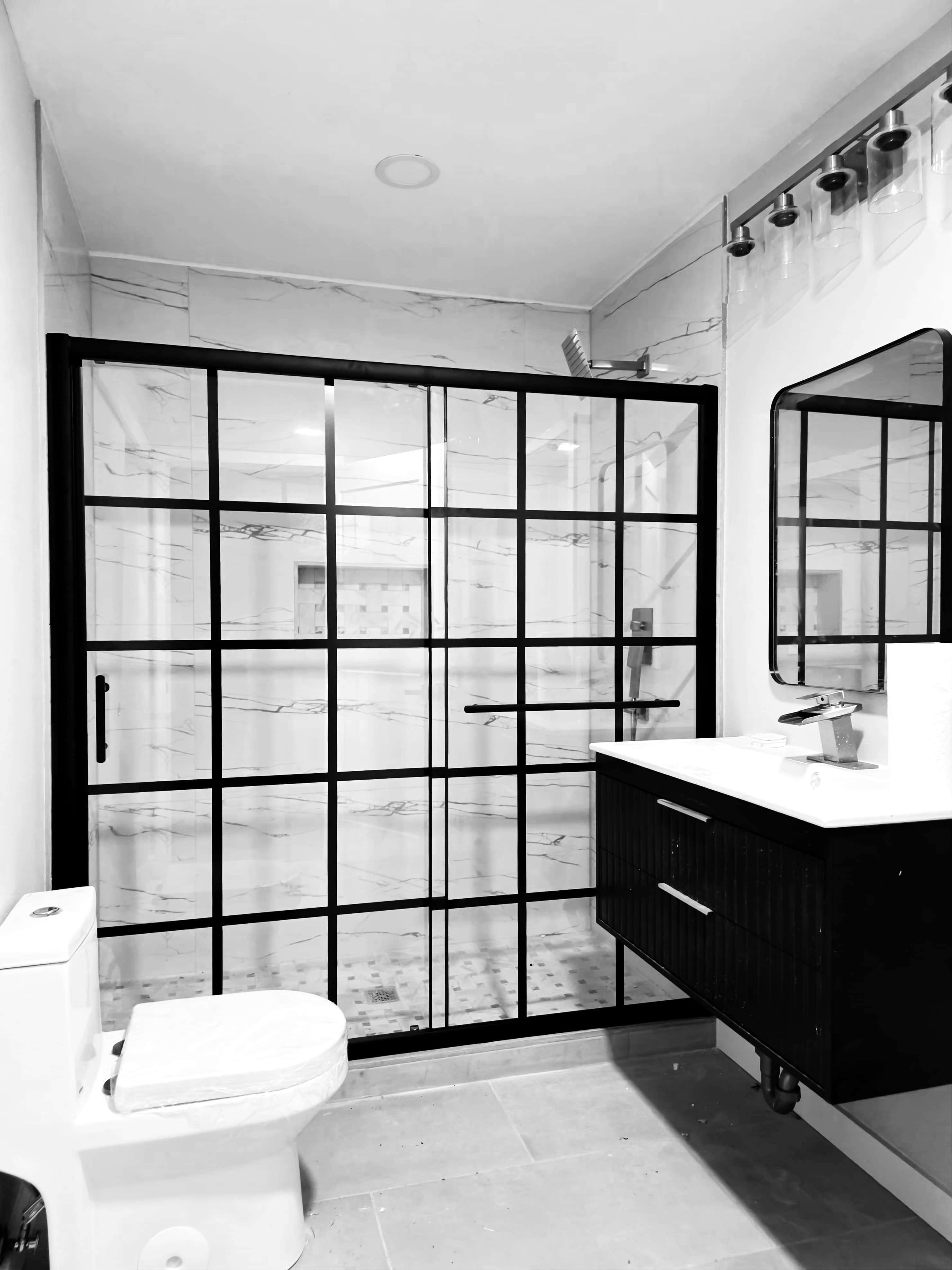 Contemporary bathroom with black grid shower door, marble walls, dark vanity, and white toilet.