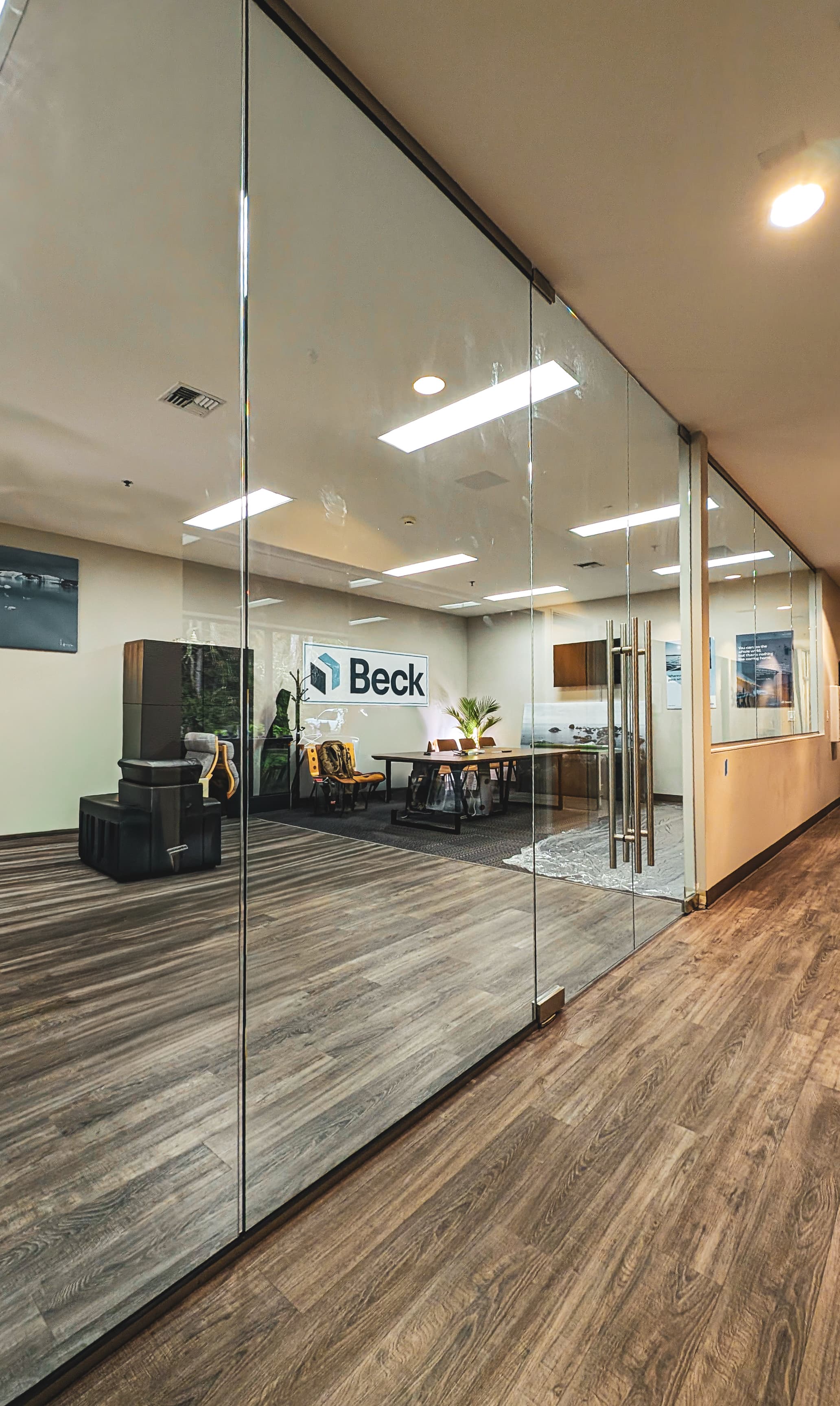 Modern office interior with glass walls, wood flooring, and a conference room featuring Beck signage.