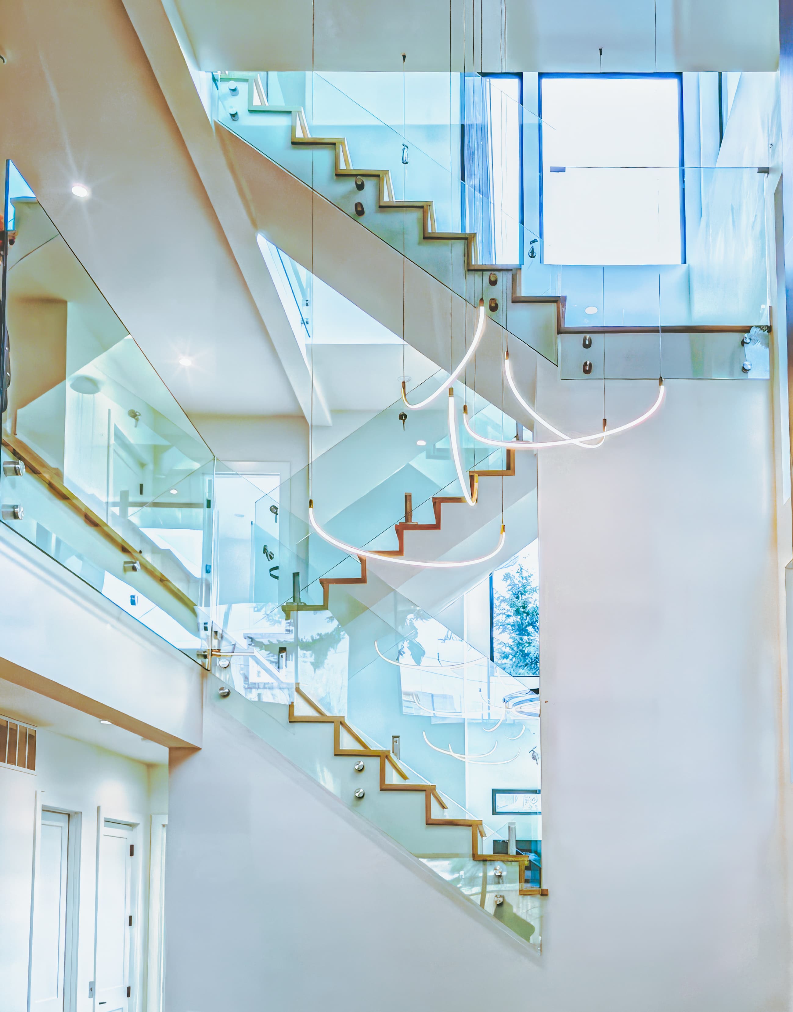 Modern multi-level staircase with glass railings and curved hanging lights in a bright interior.