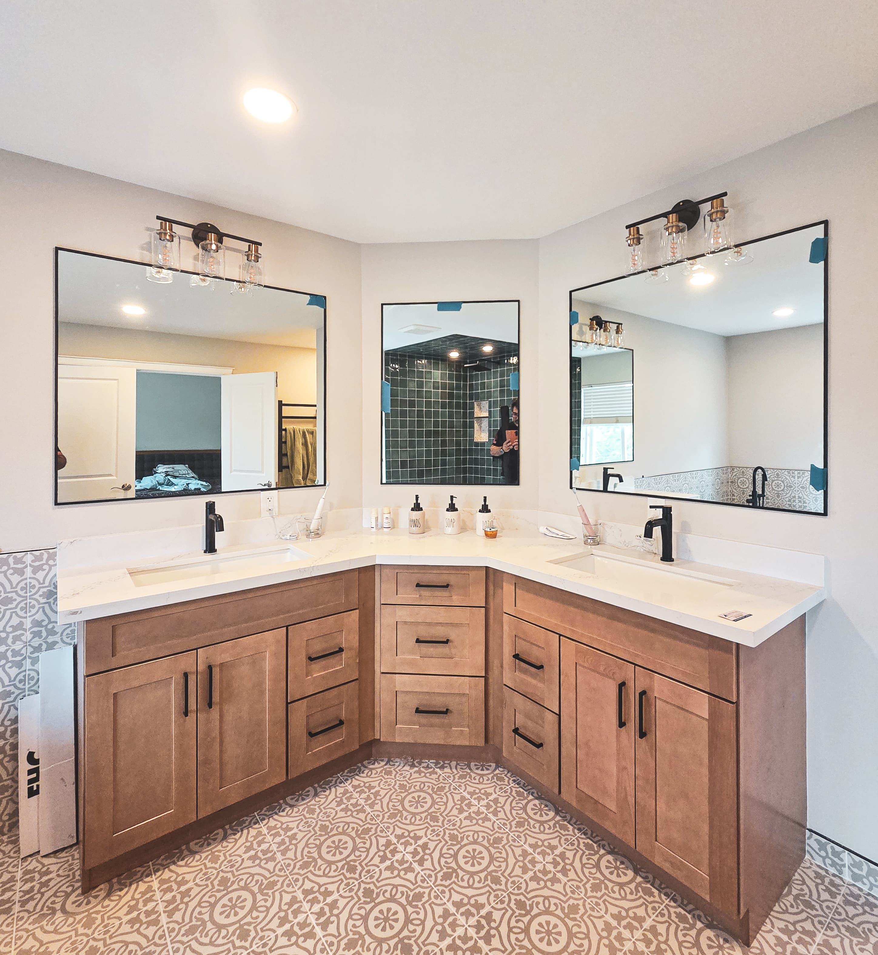 Modern corner bathroom vanity with wood cabinets, white countertops, two sinks, and patterned floor tiles.
