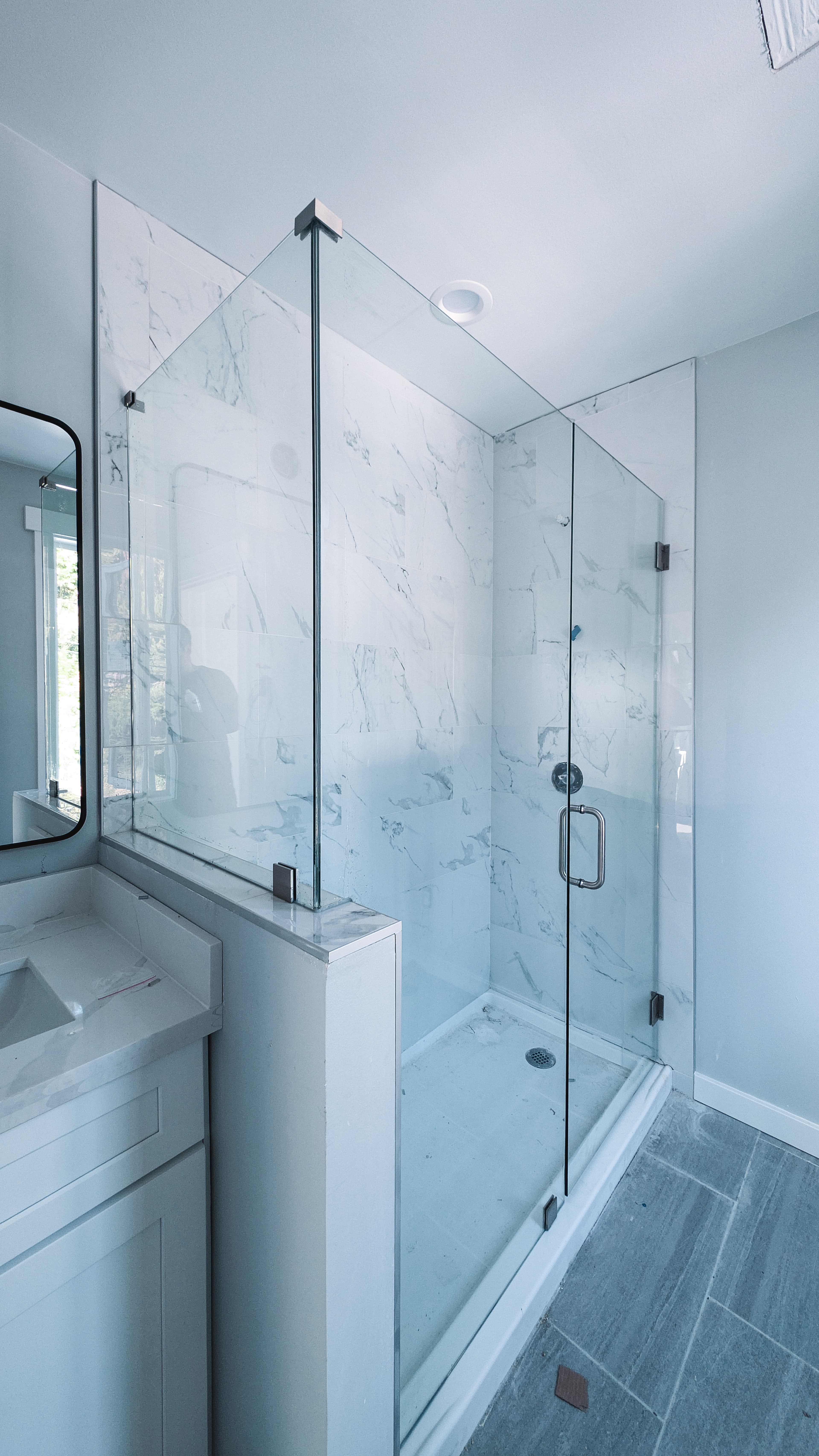 A glass-enclosed walk-in shower with white marble tiles next to a white bathroom vanity.