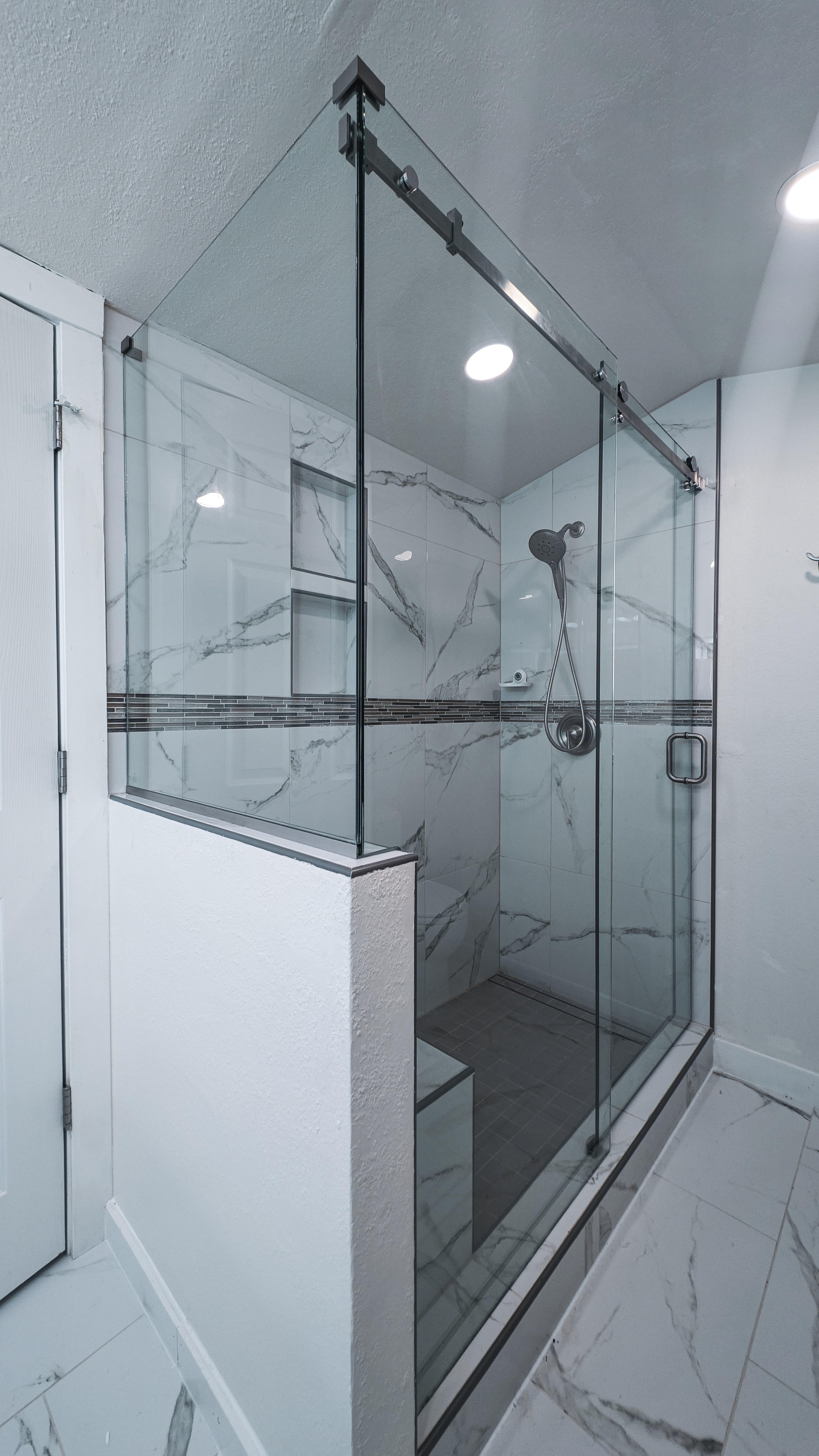 Modern walk-in shower featuring glass doors, white marble tile walls, and a built-in bench.
