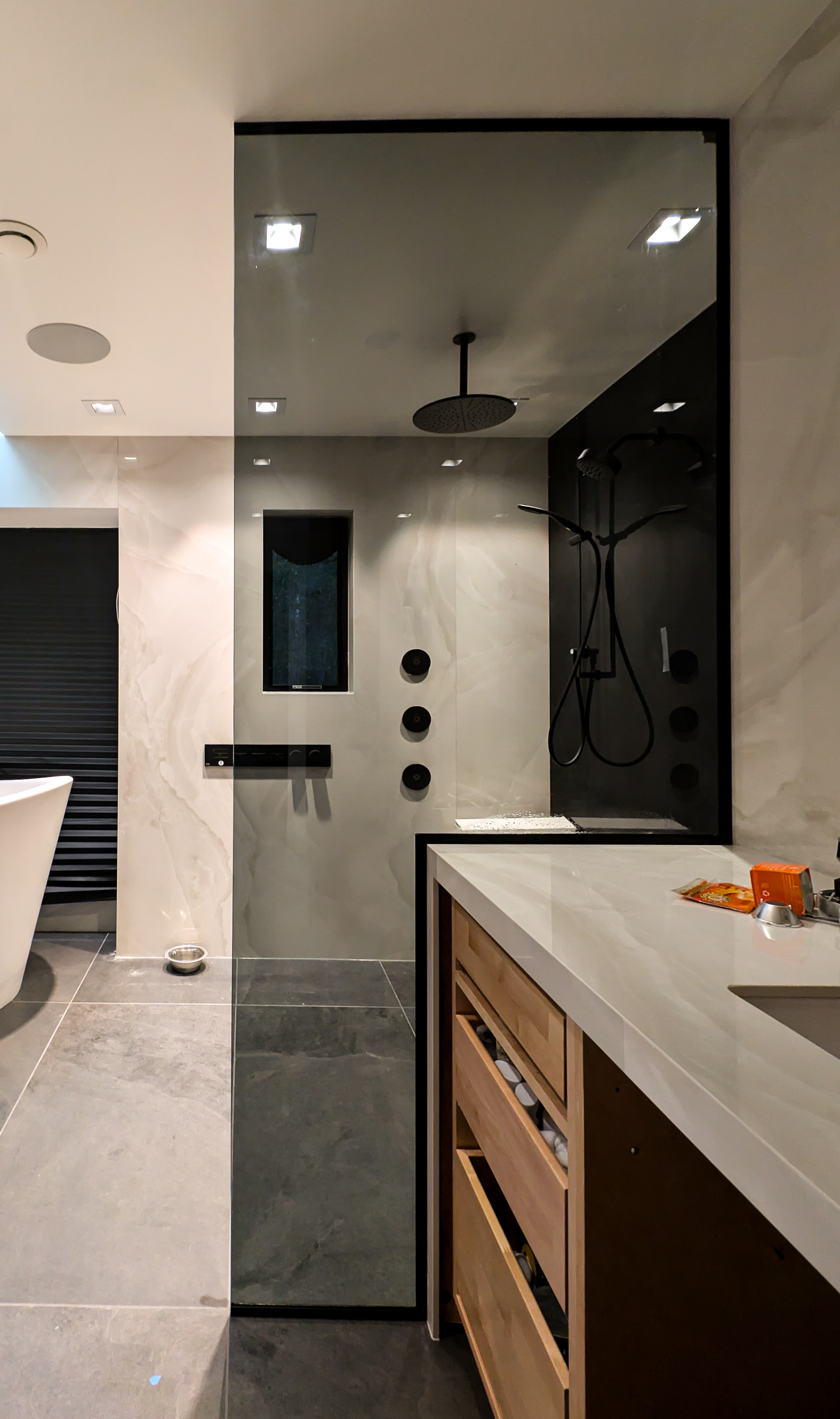 Sleek modern bathroom with a glass-enclosed shower, black fixtures, marble walls, and wooden vanity.